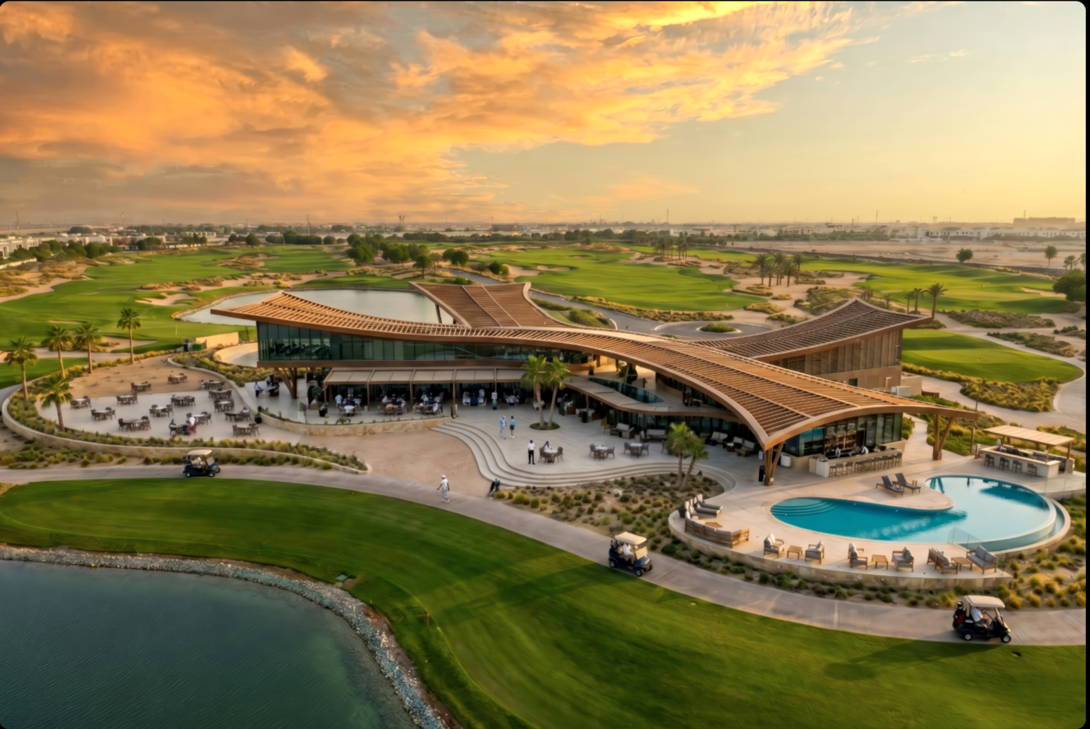 The Greens Golf Clubhouse — aerial dusk view of the curved wooden-roofed clubhouse with pool, lake and 18-hole course