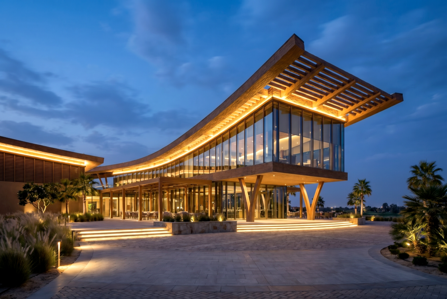 The Greens — blue-hour eye-level view of the illuminated clubhouse, lit interiors glowing under the timber roof